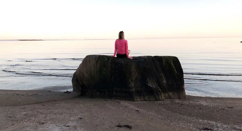 Person sitter på stor sten vid havet