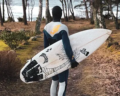 En person bär på sin surfbräda genom strandskogen